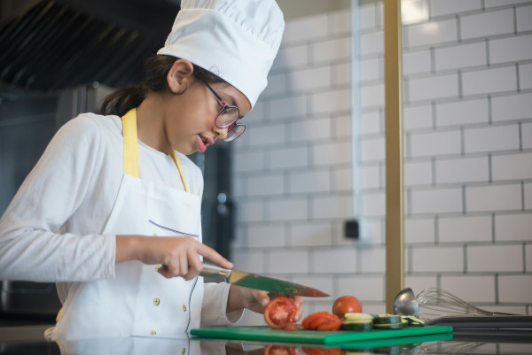 Kid in chef's hat slicing tomato with big knife