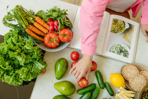 pink sleeve of child's arm reaching for a tomato with an open cookbook and veges