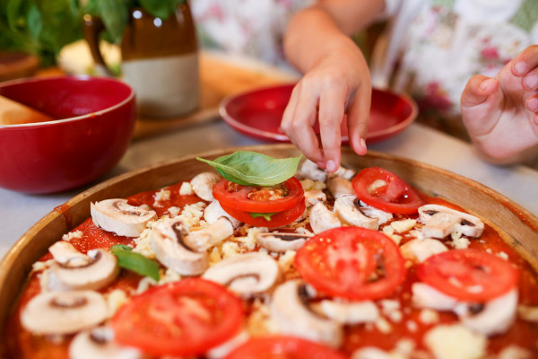 kid putting toppings on pizza