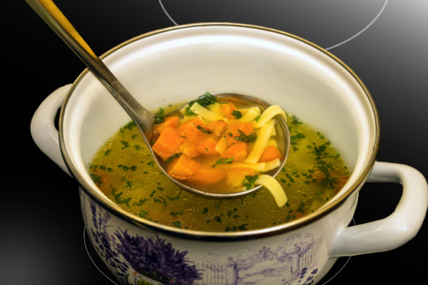 spoon scooping out carrots and noodles from mug of soup