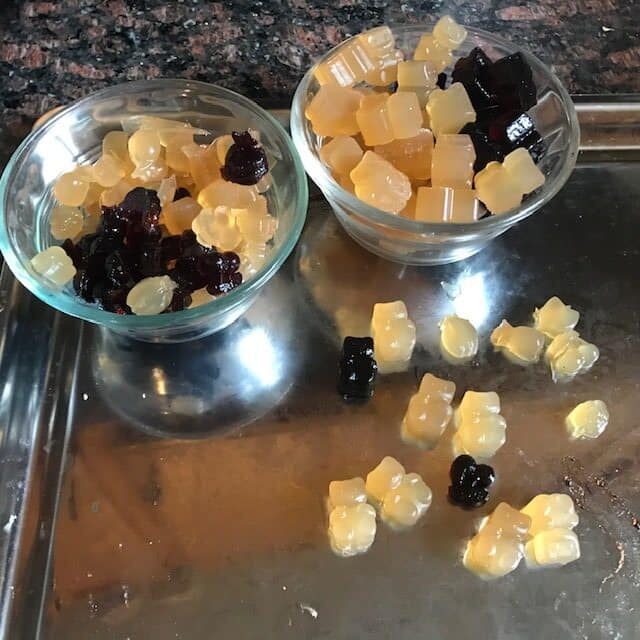two glass bowls of apple and elderberry gummies on a shiny cookie sheet with some gummies on it