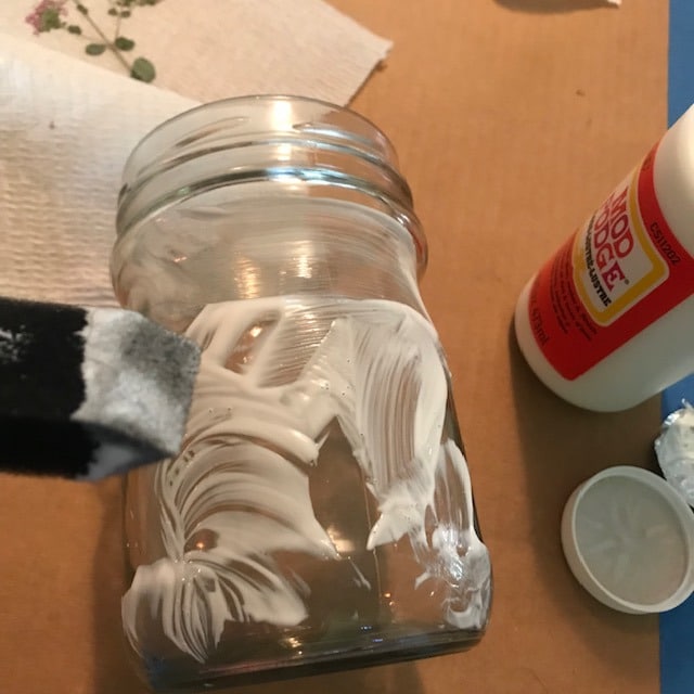mod podge being applied on a jar with a foam brush